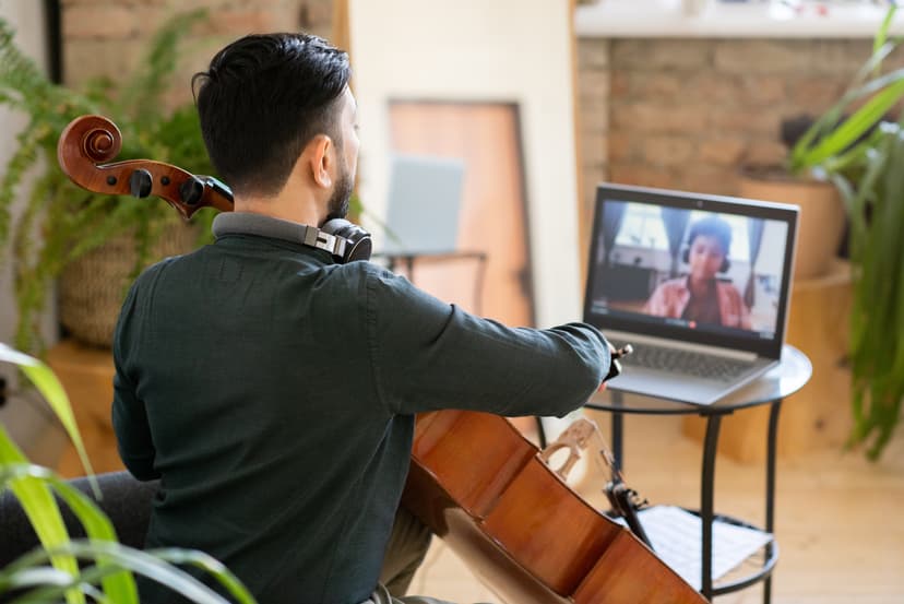 A guy practicing a cello in front of a computer